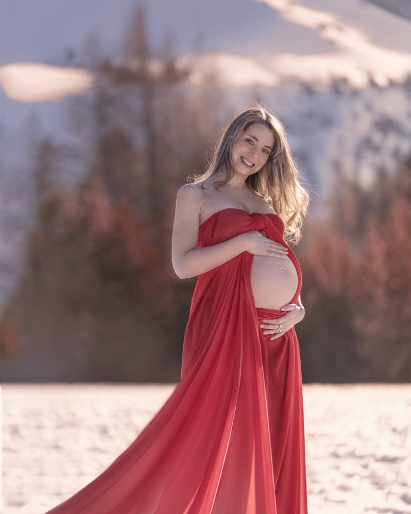 embarazada feliz en la montaña nevada con vestido rojo